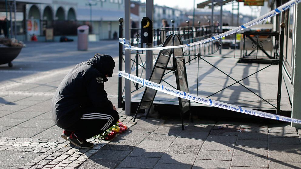 En man lägger blommor vid polisens avspärrningar utanför Vår krog och bar på Vårväderstorget i Göteborg.