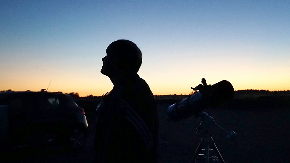 Man i profil i solnedsgången, en stjärnkikare i bakgrunden