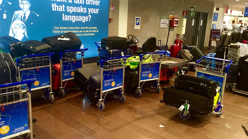 Bagagevagnar fyllda med bagage står vid en vägg.