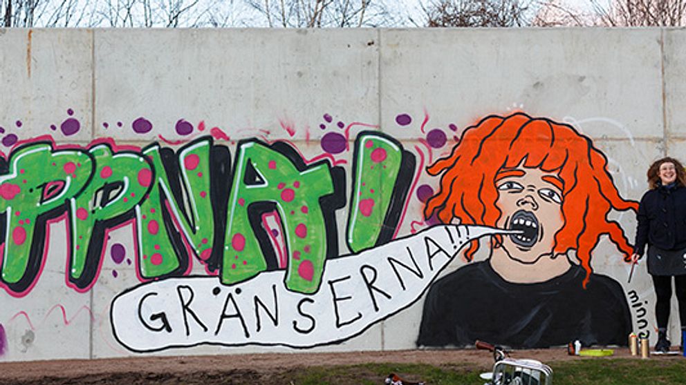 Halmstadkonstnären Minna Svensson intill det verk hon gjorde på Halmstadväggen i samband med väggens öppnande hösten 2015. Verket är ett självporträtt och i kombination med graffitin intill lyder texten ”Öppna gränserna”.