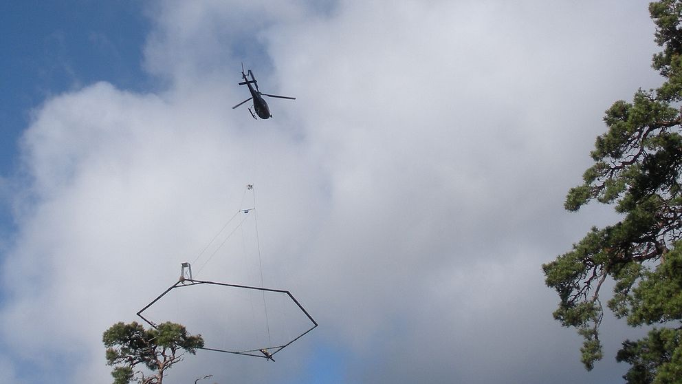 En helikopter med en stor ram som hänger under.