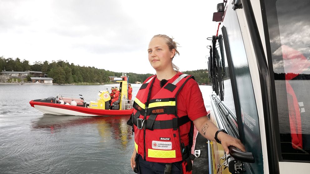 Sjöräddaren Ella Sjöberg i flytväst, står vid en båt med en räddningsbåt i bakgrunden.