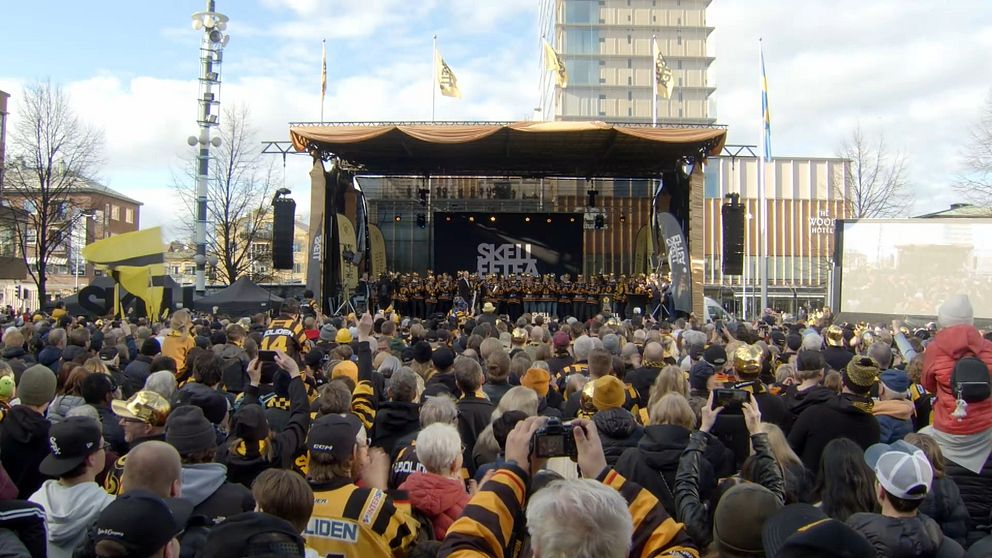 Ett stort folkhav klädda i svart och gult står framför en scen i centrala Skellefteå.