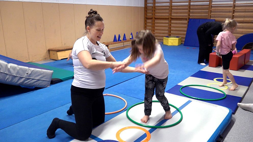 Kvinna i gympasal instruerar barn som ska göra ett hopp eller volt.