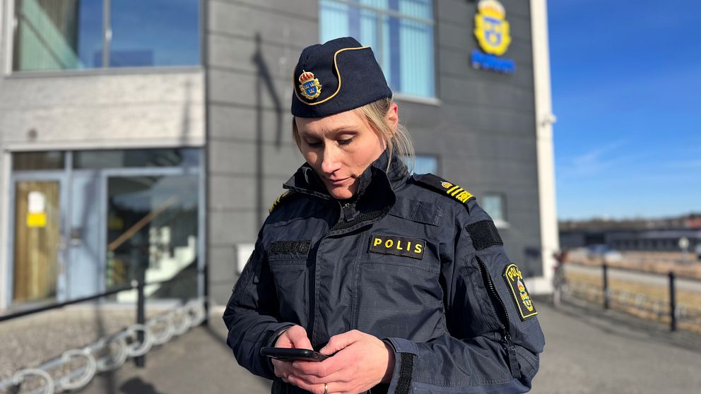 Polis i uniform utanför polisstationen med sin mobiltelefon.