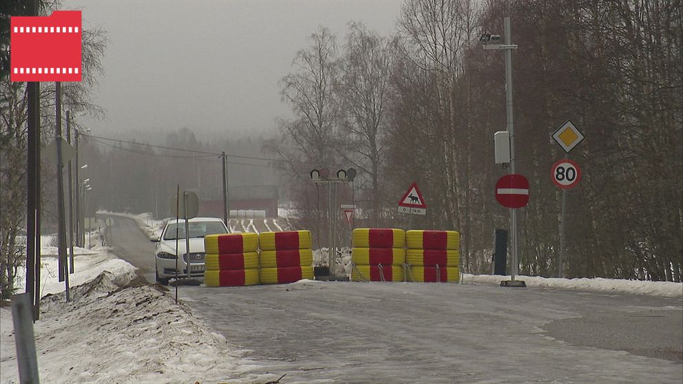 Avspärrad väg med bommar och skyltar i vintermiljö. En bil närmar sig bommarna.