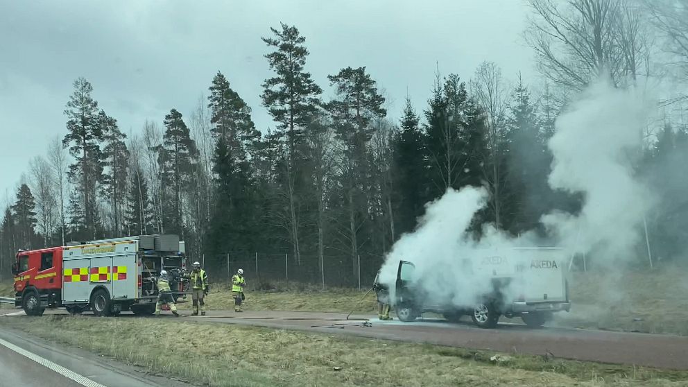 En brandbil släcker en brinnande bil som står vid sidan av en väg