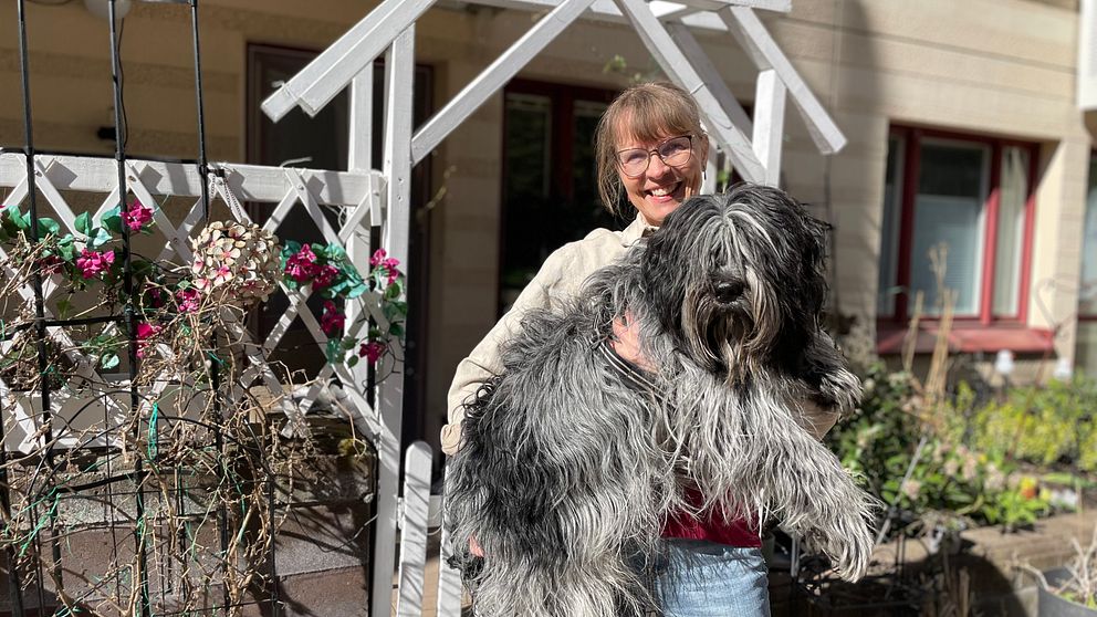 Kvinna håller i stor hund framför sitt hus.