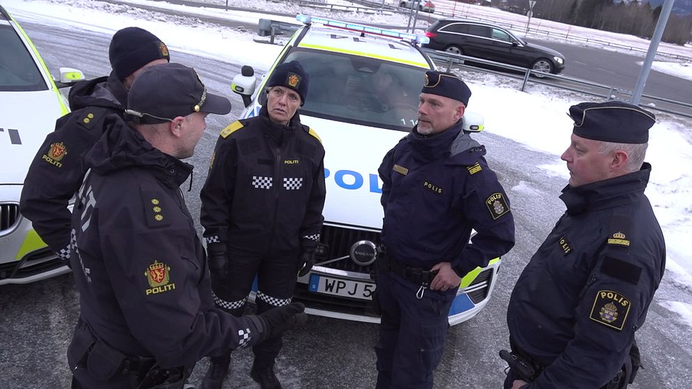 Grupp av svenska och norska poliser med polisfordon i bakgrunden. Snö och is syns på marken