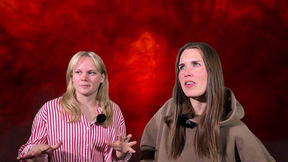 Två personer står framför en dramatisk röd bakgrund, klädda i en rosa- och vitrandig skjorta samt en gråbrun tröja. Deras ansiktsuttryck är inte synliga.