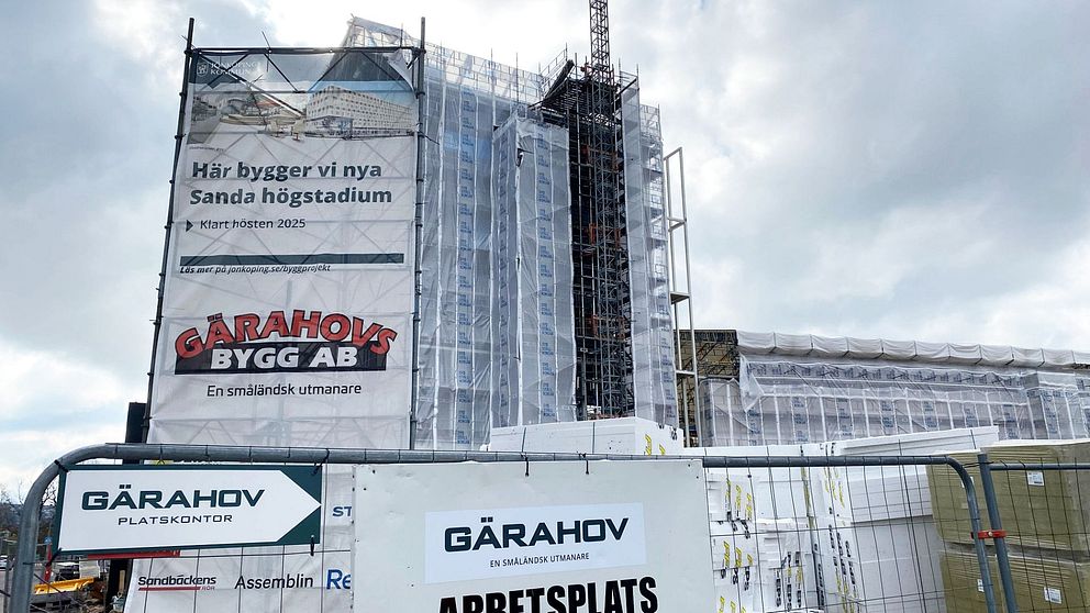Byggarbetsplats för nya Sanda högstadium under uppförande. Byggnaden är täckt med byggställningar och presenningar. Skyltar från entreprenören Garahov Bygg AB finns på stängslet framför byggarbetsplatsen.