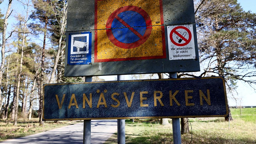 Skyltar vid en väg med information om Vanaesverken. Den övre skylten visar en röd cirkel med en diagonalt svart linje som indikerar förbud mot parkering. Intill finns en symbol för TV-övervakning och en skylt som betonar att området är övervakat och välkomnar besökare.