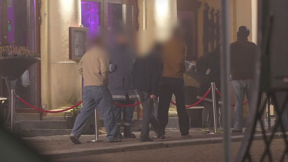 Personer med suddiga ansikten samlas utanför en nattklubb på kvällen.