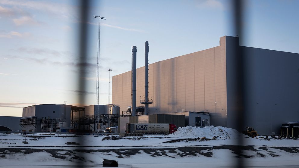 Industribyggnad inhägnad, med snö på marken och solnedgång i bakgrunden.