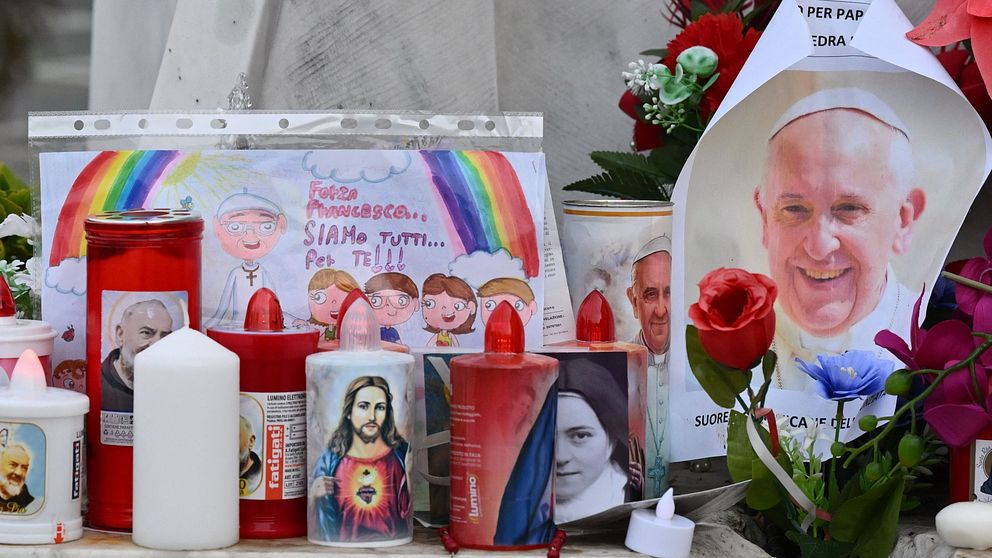 Blommor och tända ljus vid ett minnesmärke med religiösa bilder och teckningar av barn.