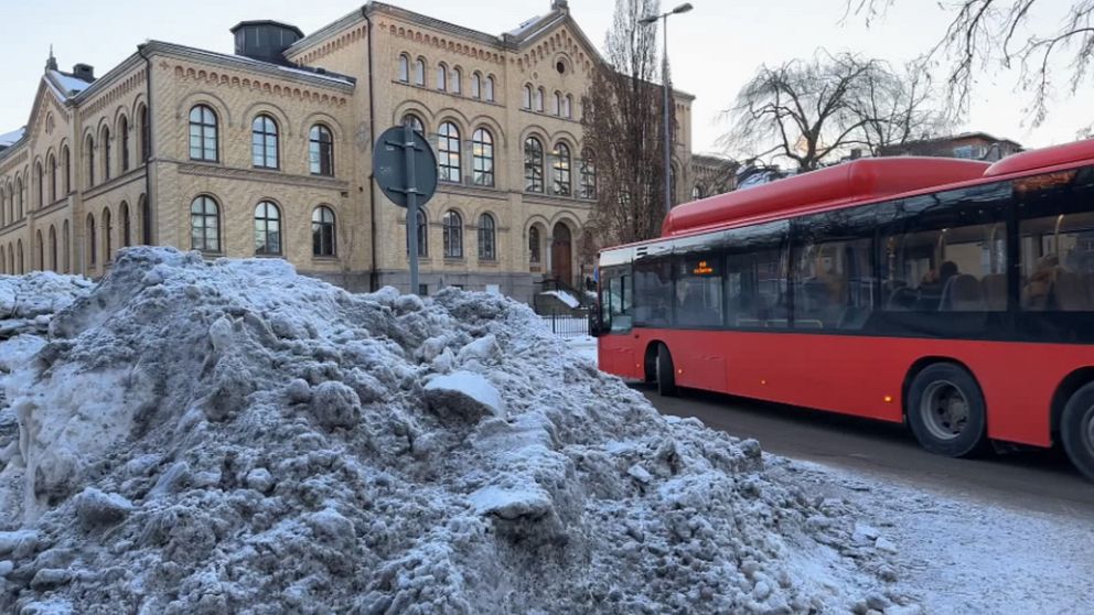 Röd buss som kör förbi snöhög.