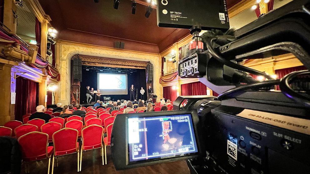 En kamera dokumenterar ett möte som pågår i en teaterlokal.