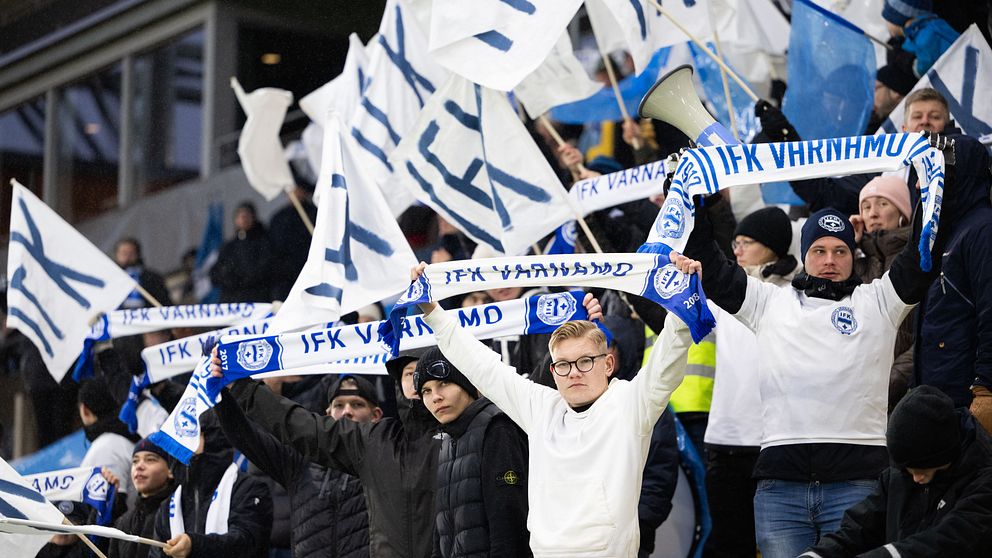 IFK Värnamo-fans viftar med flaggor och halsdukar på läktaren under en fotbollsmatch.