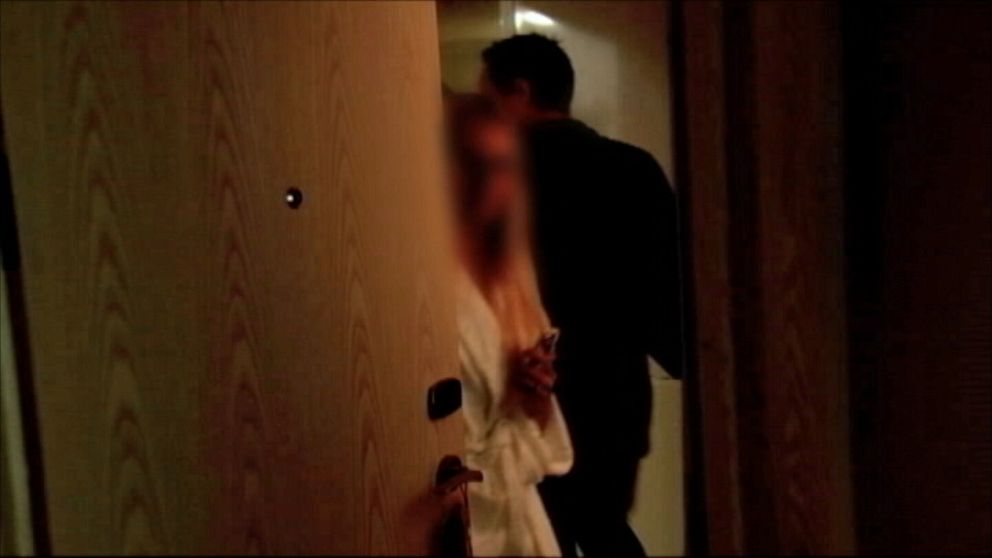 En kvinna i vit morgonrock och utsuddat ansikte stängerytterdörren, samtidigt som en man går in i lägenheten.