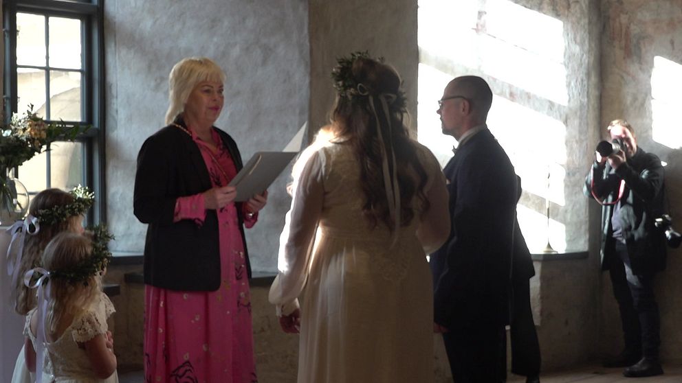 Brudpar samt vigselförrättare på Kalmar slott. Brudparet står framför ett fönster och solen skiner in.