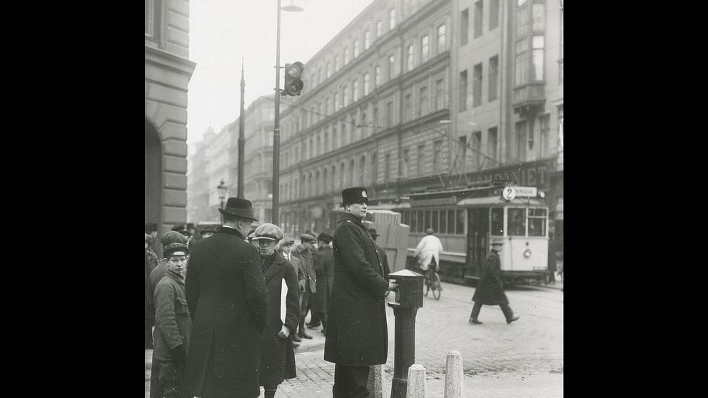Svartvit gatubild med spårvagn och fotgängare i historisk stadsmiljö i Stockholm.