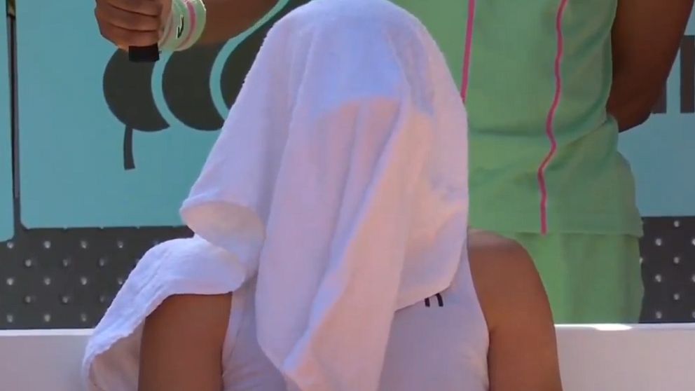 Tennis­spelare svalkar sig med en handduk över huvudet under paus vid sidlinjen.