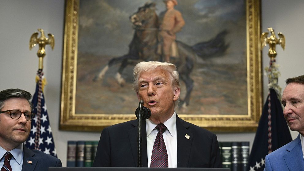 Tre personer framför målning av ryttare. Amerikanska flaggor syns bredvid.