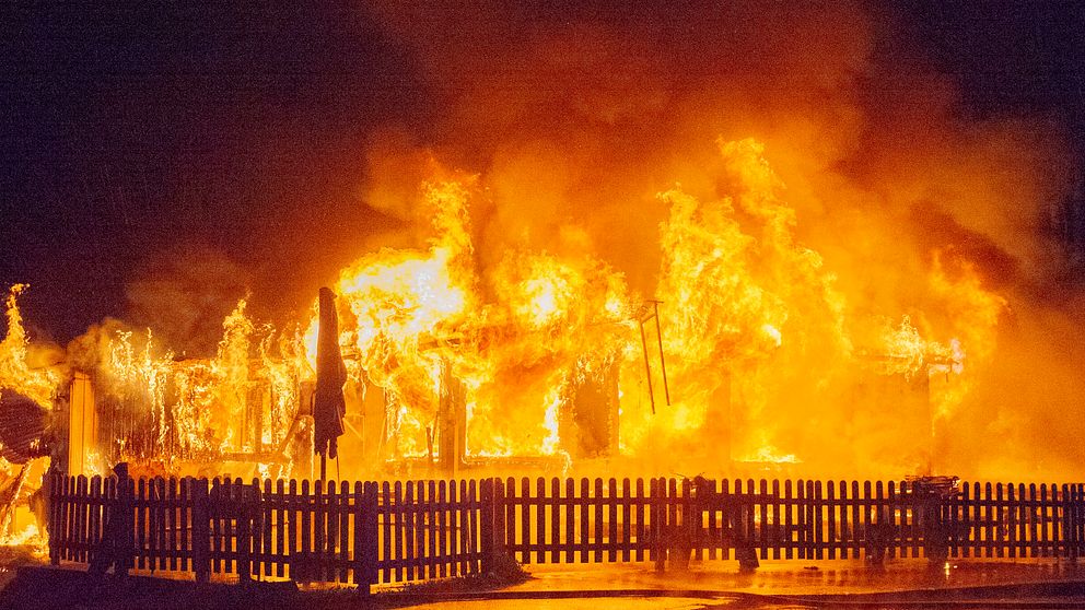 Eldslågor slukar en byggnad bakom ett staket under en kraftig brand på natten.
