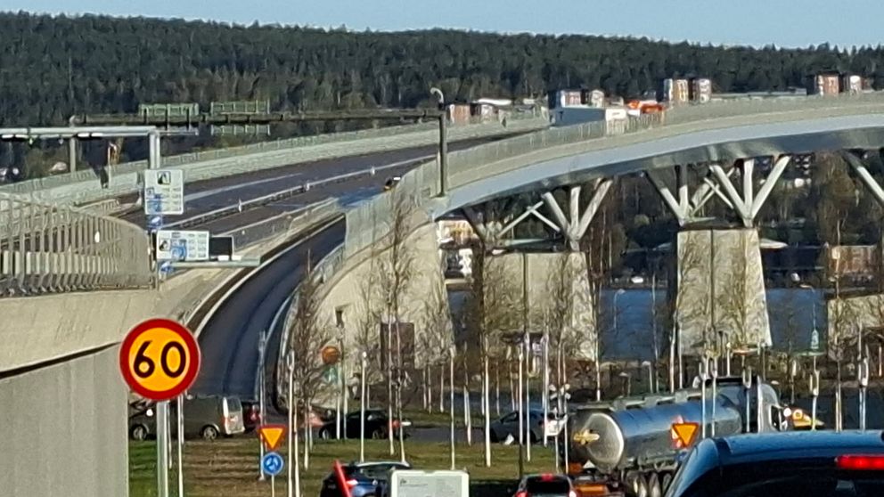 Motorvägsbro med 60-skylt, bilar i förgrunden och skog i bakgrunden.