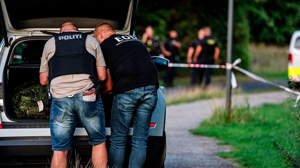 Två civilklädda poliser med skyddsväst står vid en bil.
