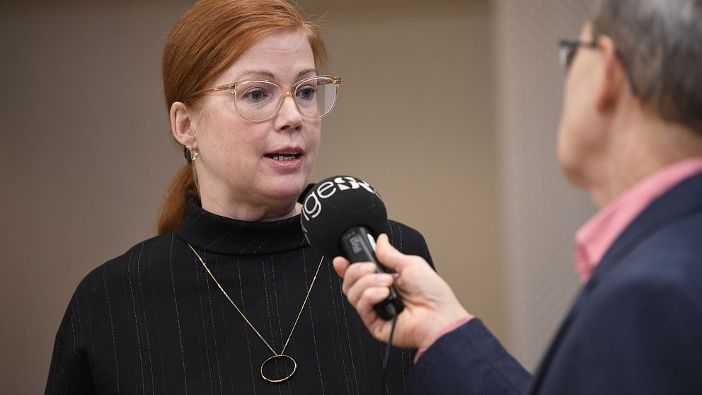 Reporter intervjuar Anna Starbrink med mikrofon i en inomhusmiljö.