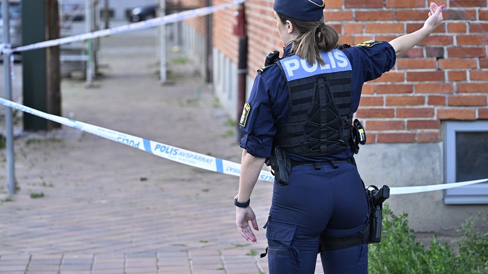Polisavspärrning vid tegelbyggnad, polis dirigerar trafik.