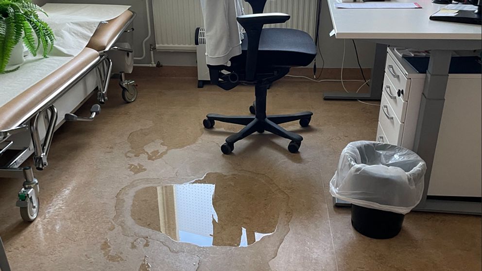 Vattenläcka i ett kontor med skrivbord och kontorsstol, samt pöl på golvet.