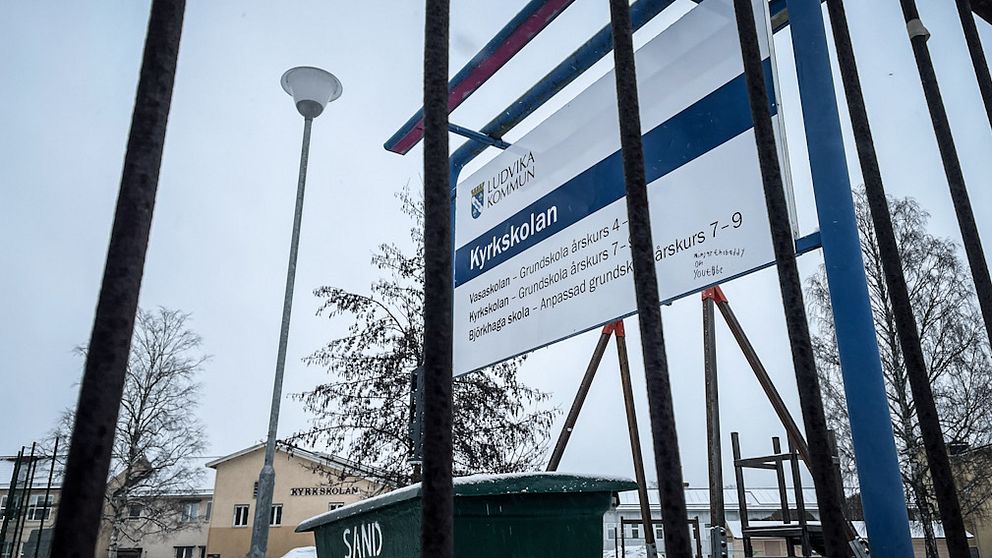 En informationsskylt utanför Kyrkskolan i Ludvika syns genom ett staket.