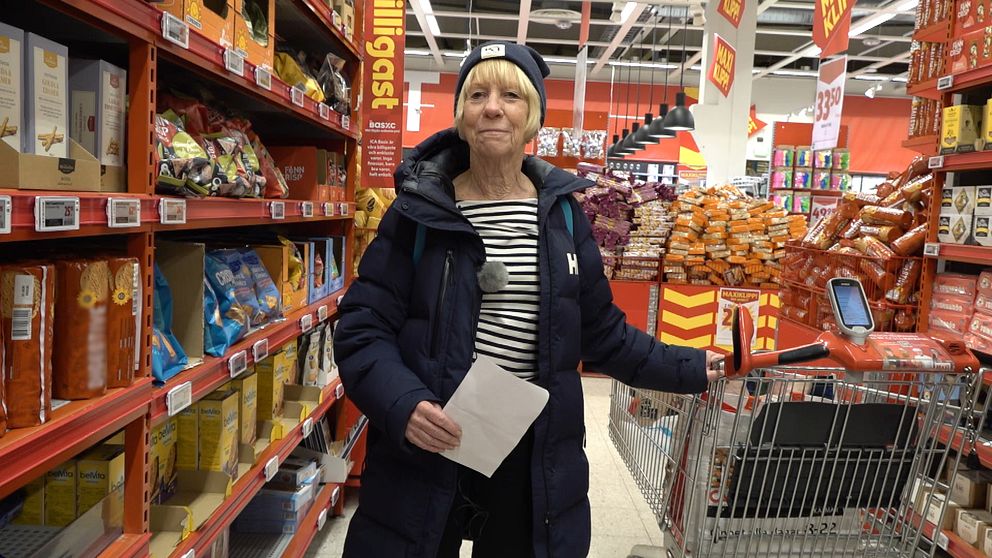 En kvinna står i en gång i en matvarubutik vid en kundvagn