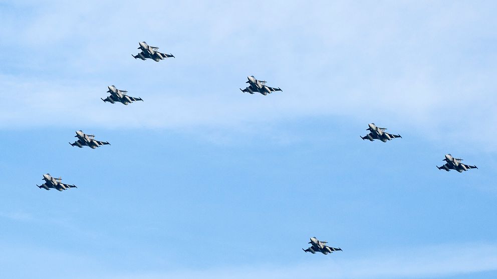 Flera stridsflygplan i formation flyger över en blå himmel. Flygplanen är arrangerade i en cirkulär formation, vilket skapar en imponerande visuell effekt.