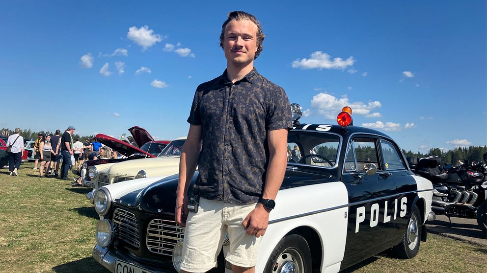 Arvid Jonsson, står i ett soligt Östersund framför en gammal polisbil från 68.