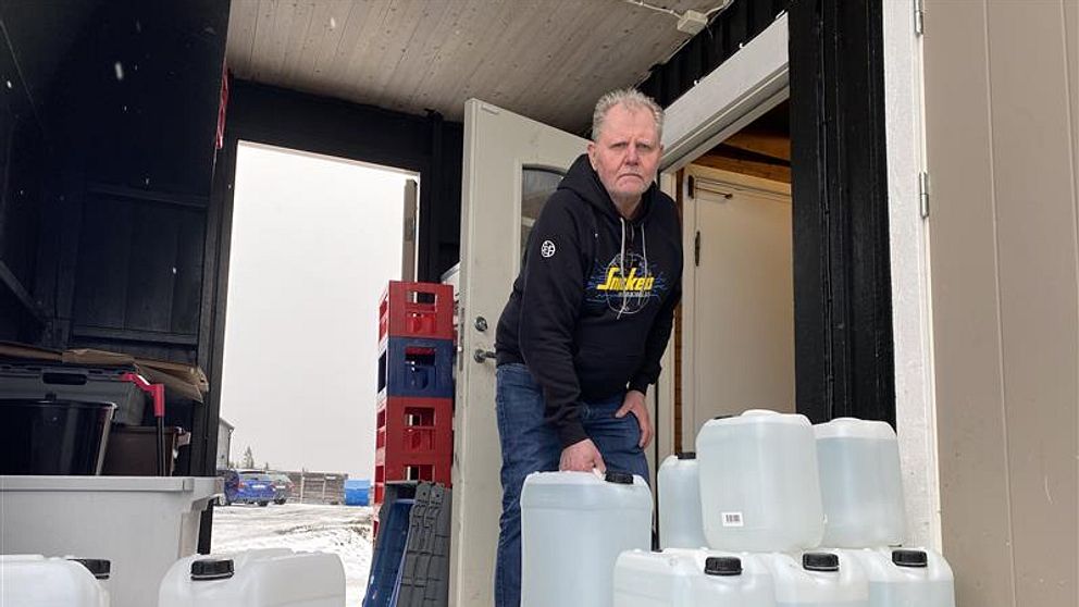 Man bär flera plastdunkar ut från en byggnad.