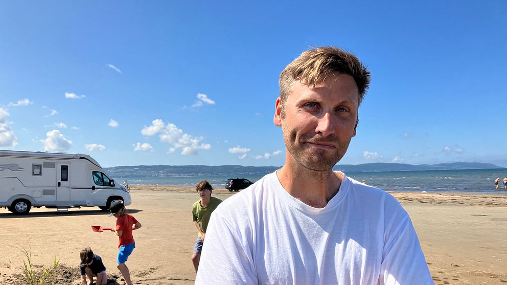 Pappan Daniel Norling på stranden i Laholm med lekande barn i bakgrunden.