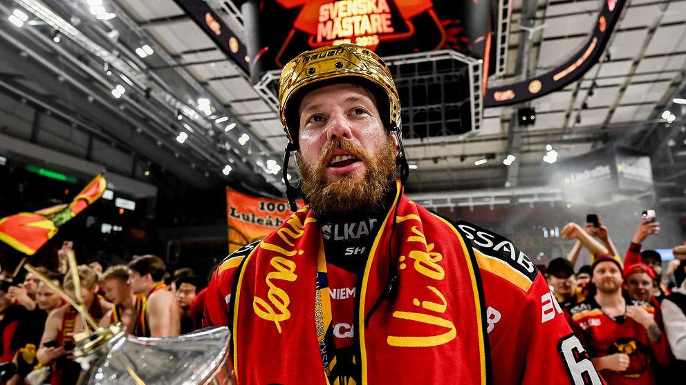 En hockeyspelare firar med pokal framför jublande supportrar i ishallen.