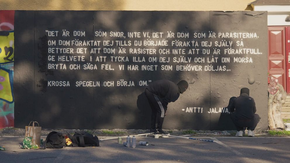 två graffitikonstnärer färdigställer ett citat på väggen