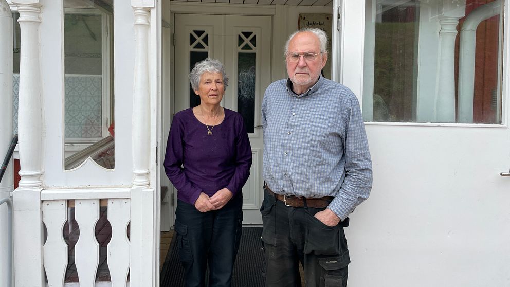 En kvinna och en man står utanför en vit verandadörr, kvinnan i lila tröja, mannen i blå skjorta.