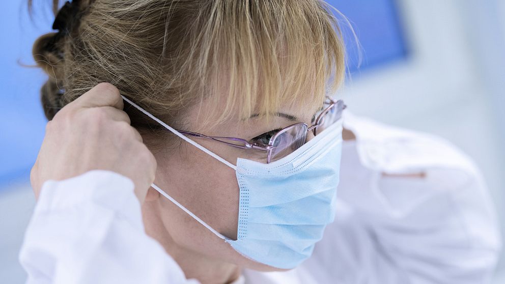 Kvinna i sjukhuskläder sätter på sig ett munskydd.