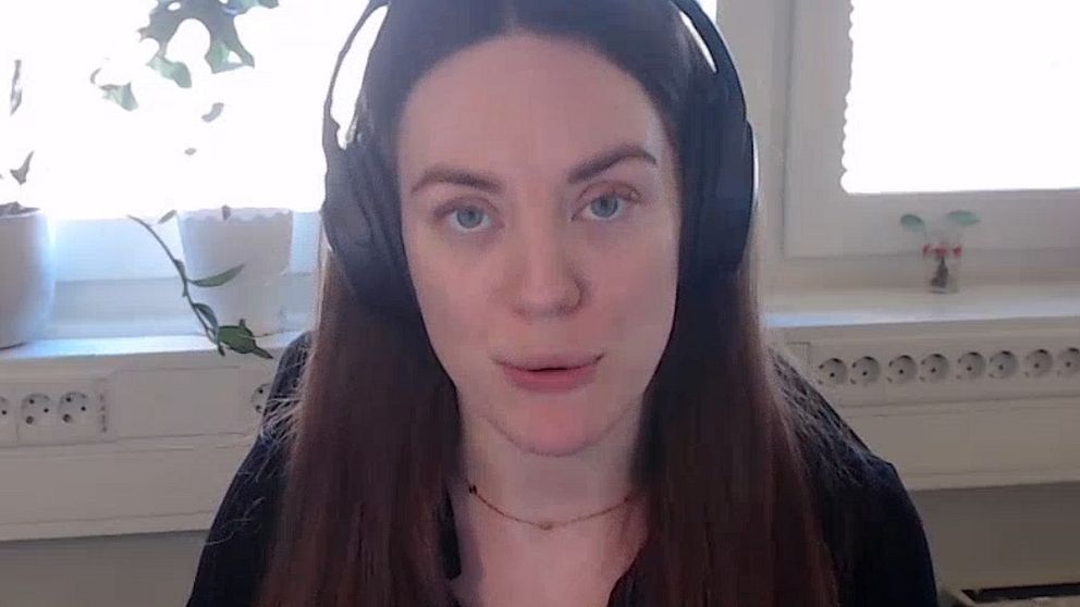 Person i svart tröja och hörlurar sitter framför ett vitt fönster med växter på fönsterbrädan.