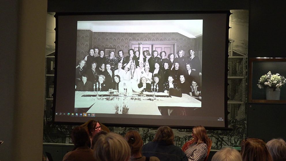 Bild på kvinnor i grupp på storskärm, inne på stadsmuseet