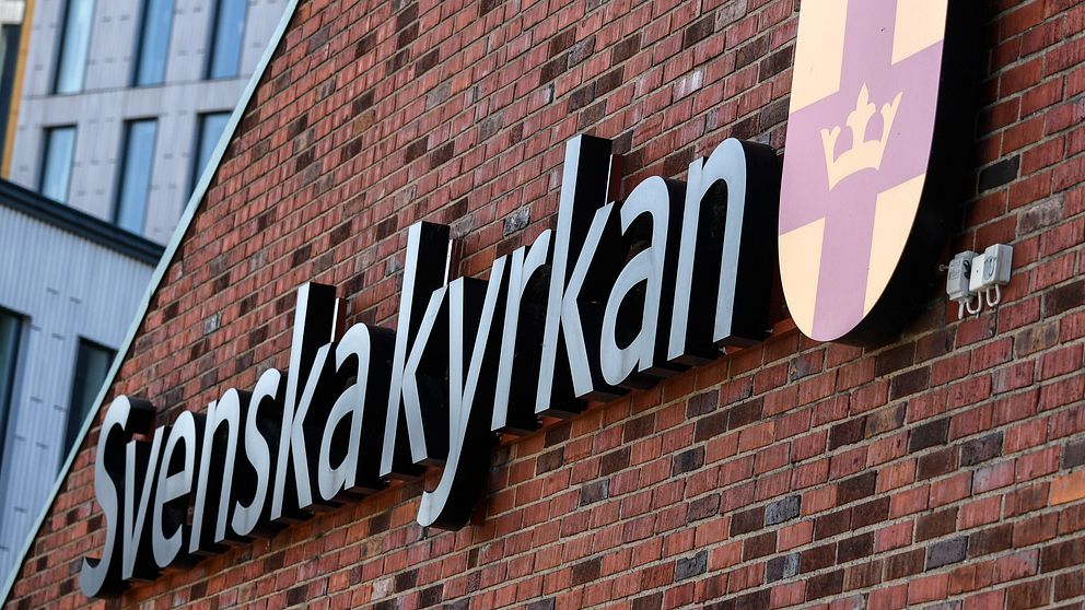 Svenska kyrkans logotyp och sköld på en tegelvägg.