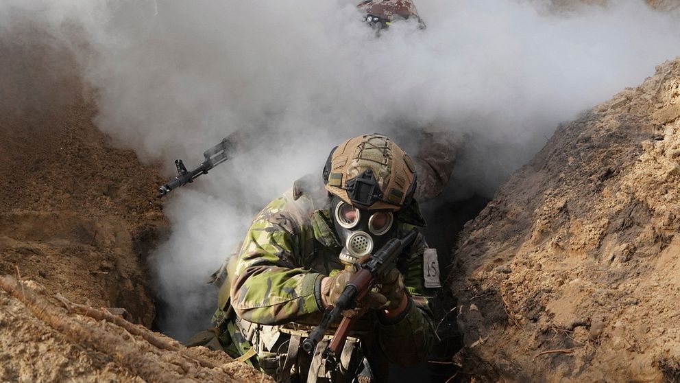 En soldat i gasmask hukar sig i en skyttegrav.