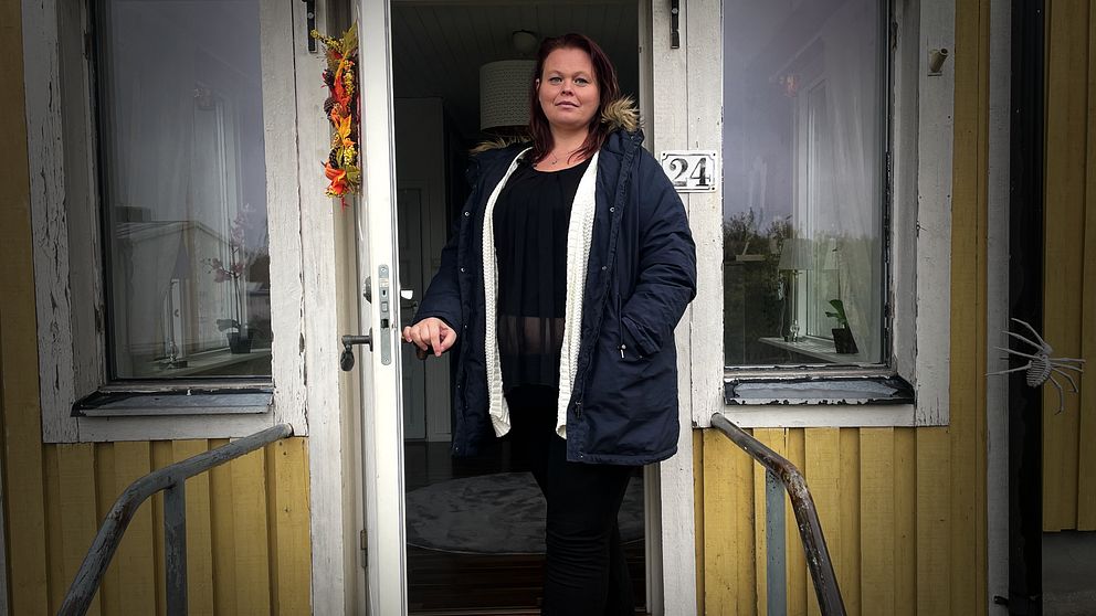 Kvinna håller upp dörren till ett gult hus.