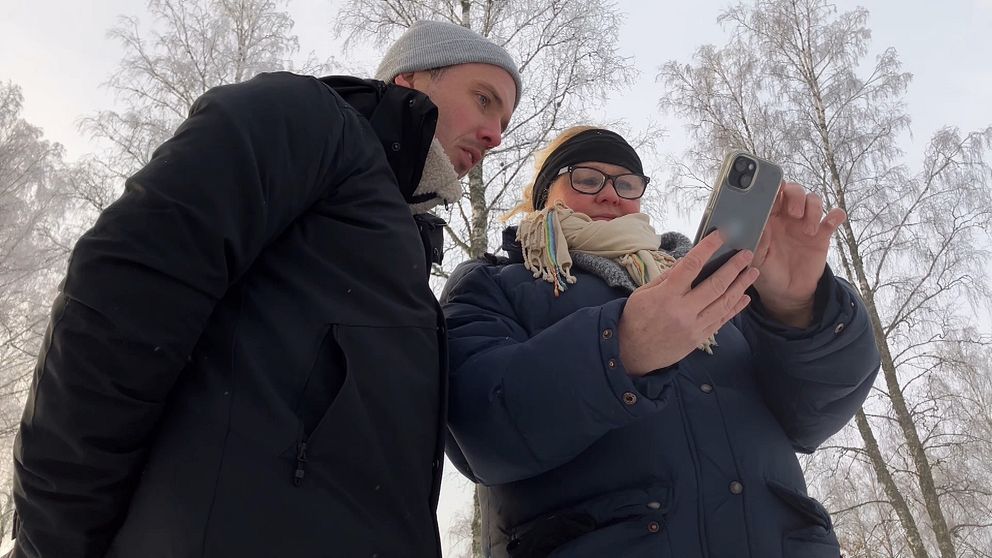 En man och en kvinna som står och tittar ner i en mobiltelefon. Bilden är tagen snett underifrån.