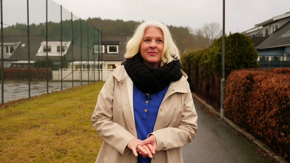 Cecilia Wendin i blont hår, beige kappa, blå tröja, jeans, går bland radhus i Göteborg.